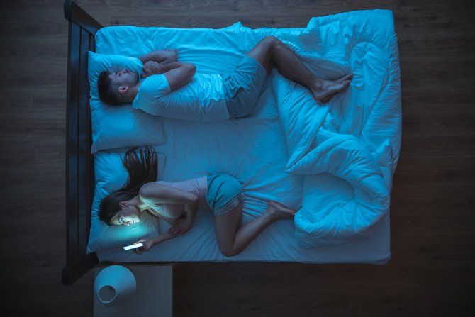 жена использует смартфон в постели, пока муж спит