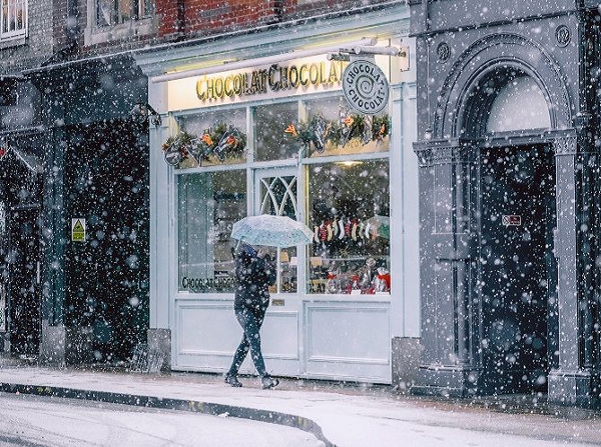 Прогуливаясь мимо кафе и магазинов на Рождество, пока идет снег