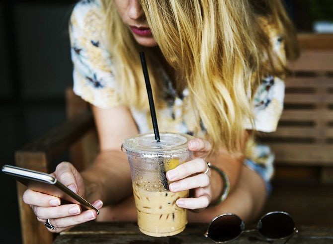 Женщина пьет кофе и смотрит на iPhone