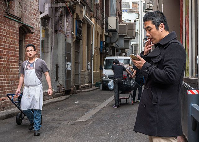 Человек курит сигарету по телефону в переулке